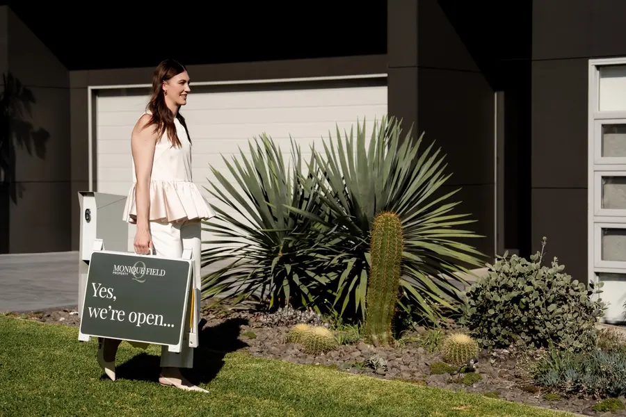 Monique Field carrying an open home sign to the front of a house